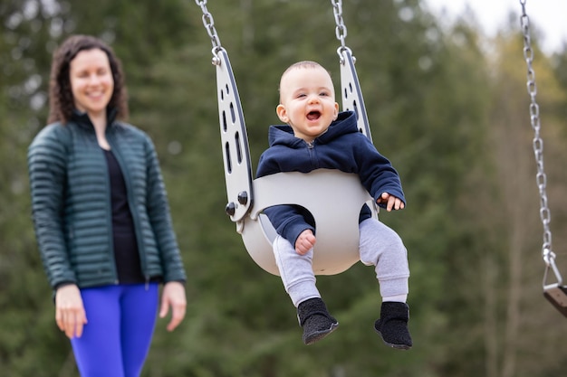 Photo un petit garçon caucasien sur une balançoire avec sa mère à l'extérieur du parc