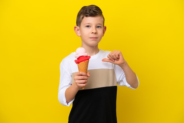 Petit garçon caucasien avec une glace au cornet isolé sur fond jaune fier et satisfait