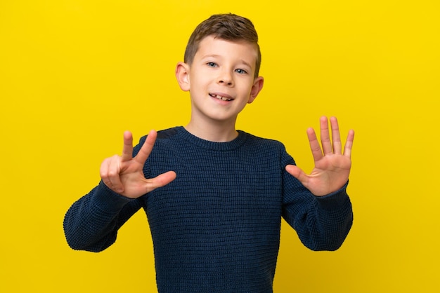 Petit garçon caucasien isolé sur fond jaune comptant huit avec les doigts