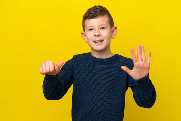 Petit garçon caucasien isolé sur fond jaune comptant six avec les doigts