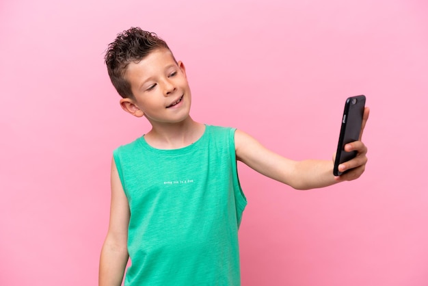 Petit garçon caucasien isolé sur fond rose faisant un selfie