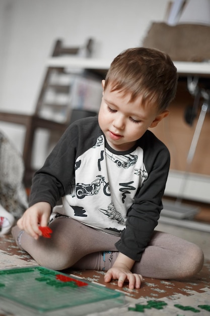 Petit garçon caucasien jouant à un jeu de société sur le sol dans sa chambre, photo de style de vie à la maison