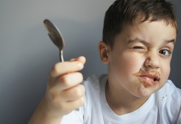 Petit garçon caucasien mangeant du chocolat mur gris mignon gosse heureux recouvert de chocolat concept de l'enfance