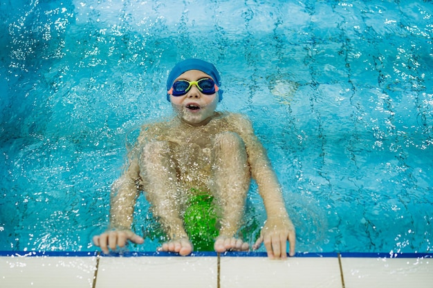 Un petit garçon caucasien portant des lunettes commence à nager le dos dans une piscine. photo de haute qualité