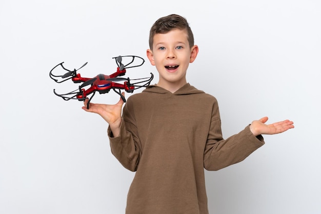 Petit garçon caucasien tenant un drone isolé sur fond blanc avec une expression faciale choquée
