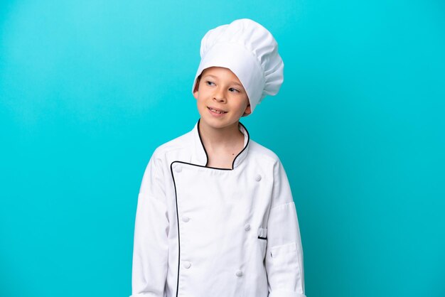 Petit garçon chef isolé sur fond bleu regardant sur le côté et souriant