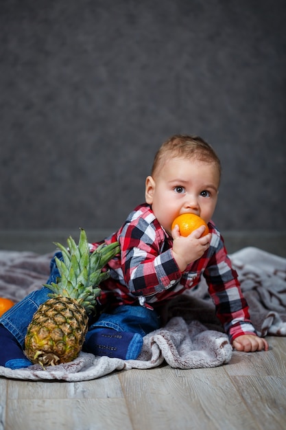 Le petit garçon en chemise est assis sur le plaid et tient le fruit