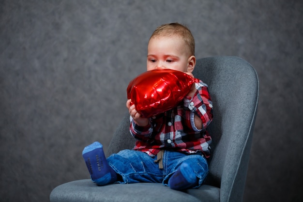 Un petit garçon en chemise joue avec un ballon en forme de coeur