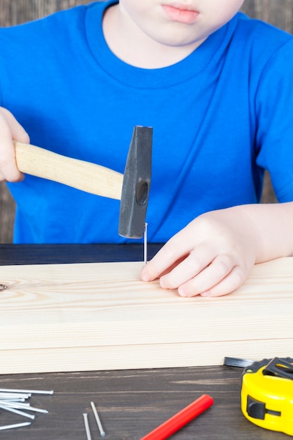 Un petit garçon construit un nichoir en bois, martelant des clous dans la planche