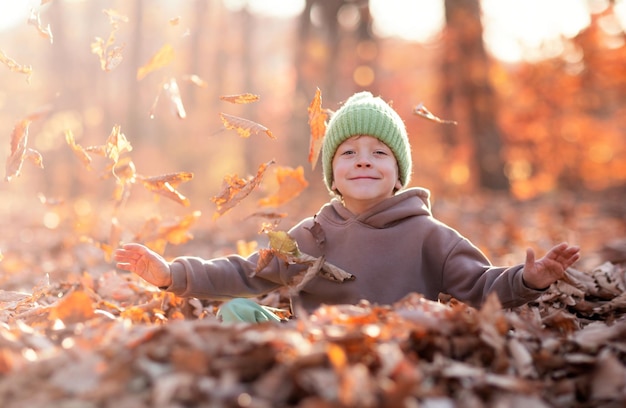 un petit garçon content assis dans une pile de feuillage d'automne