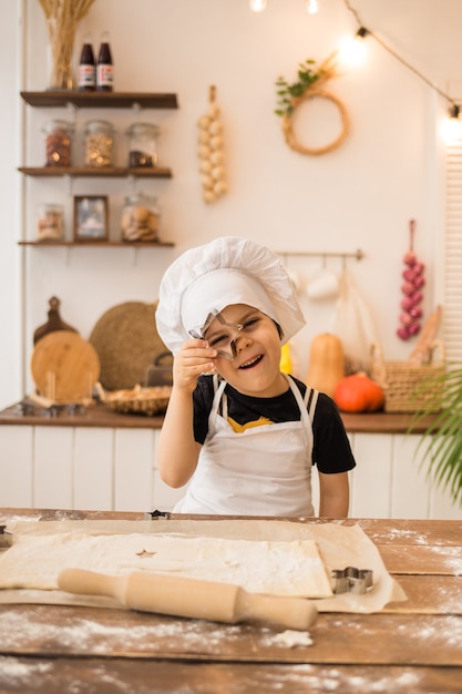 Un petit garçon en costume de chef s'amuse dans la cuisine avec un emporte-pièce