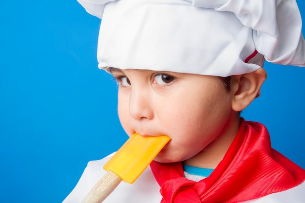 Le petit garçon en costume de cuisinier. adorable petit garçon en toque et tablier souriant à la caméra dans la cuisine. garçon en toque