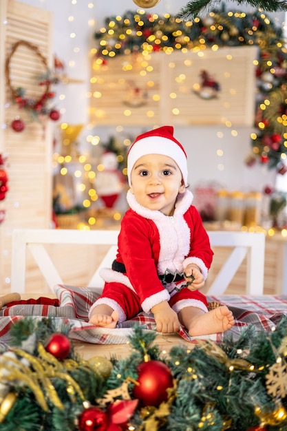 Un petit garçon en costume de Père Noël est assis sur une table dans la cuisine festive du Nouvel An à la maison un enfant heureux célèbre Noël et le Nouvel An à la maison