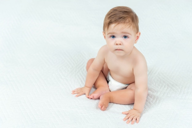 Petit garçon en couche assis sur le lit dans la chambre. Portrait d'enfant mignon sur fond blanc, copiez l'espace.