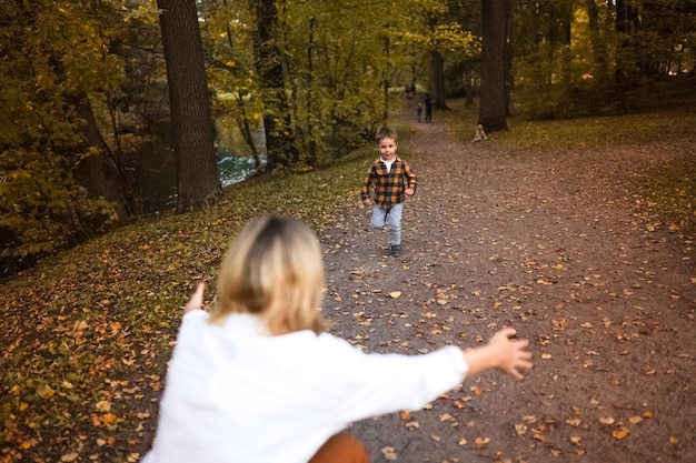 Petit garçon courant vers la mère le long de la voie couverte de feuilles mortes dans le parc d'automne