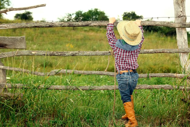 Un petit garçon cowboy au chapeau près de la clôture sur la nature
