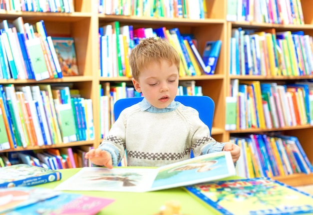 Photo un petit garçon dans la bibliothèque feuillette un livre d'images pour enfants