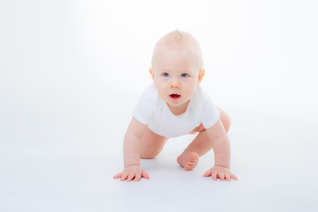 Petit garçon dans un body blanc rampant sur un fond blanc