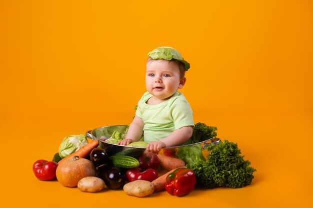 Petit garçon dans un body vert est assis dans un bol en métal avec des légumes. concept de produit agricole