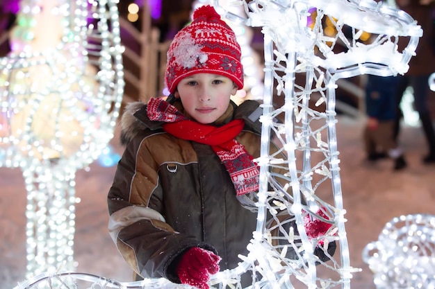 Un petit garçon dans un bonnet rouge tricoté sur le fond d'un décor urbain festif de Noël