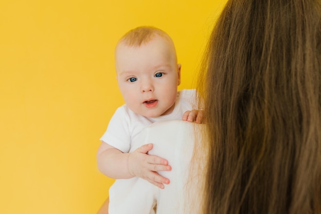 Petit garçon dans les bras de maman sur fond jaune