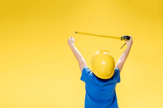 Un petit garçon dans un casque de chantier de protection mesure avec un ruban à mesurer.