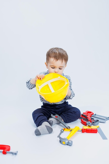 Un petit garçon dans une chemise à carreaux à l'image d'un constructeur Un garçon dans un casque de construction et des outils en plastique