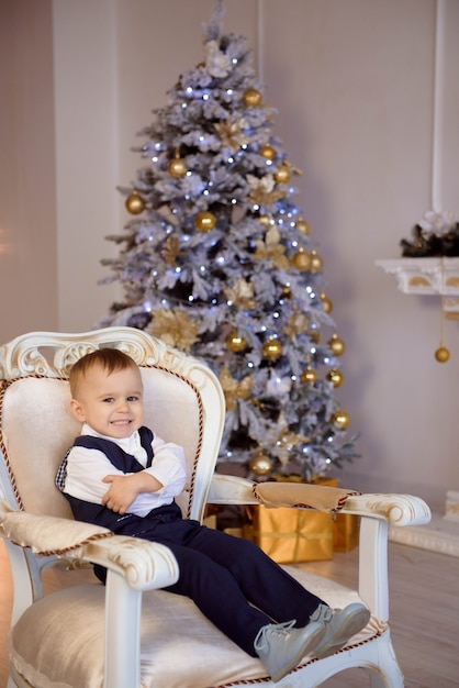 Petit garçon dans un costume attendant un Noël près de l'arbre de Noël