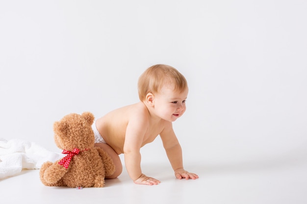 Le petit garçon dans une couche est assis sur un fond blanc avec un ours en peluche