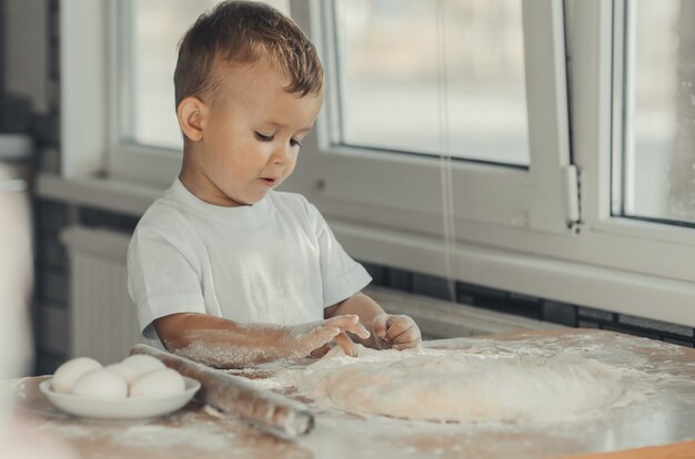 Le petit garçon dans la cuisine lui-même en t-shirt blanc pétrit dur la pâte