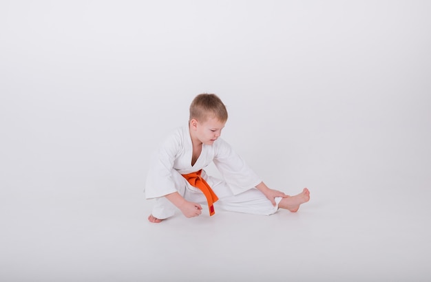 Petit garçon dans un kimono blanc avec une ceinture orange fait un échauffement sur fond blanc