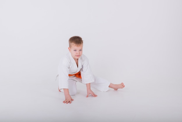 Petit garçon dans un kimono blanc fait un étirement sur un mur blanc