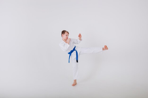 Petit garçon dans un kimono blanc pratique des coups de poing sur un mur blanc