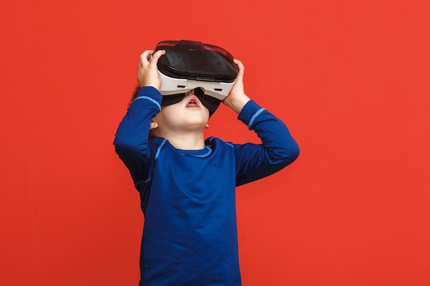 Petit garçon dans des lunettes de réalité virtuelle jouant le jeu sur un fond rouge Technologie de gadget 3D Lunettes de casque VR en carton