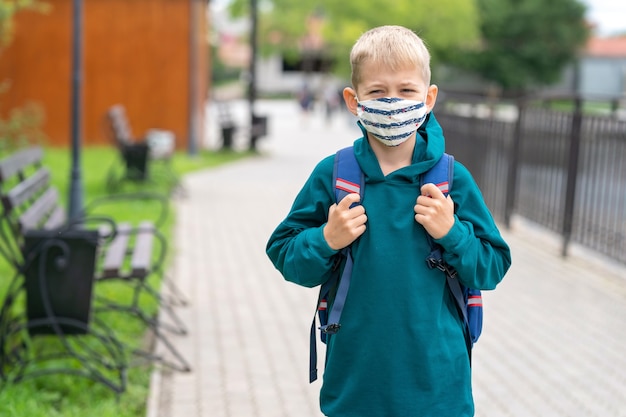 Un petit garçon dans un masque de protection sur le visage et avec un sac à dos sur les épaules Retour à l'école