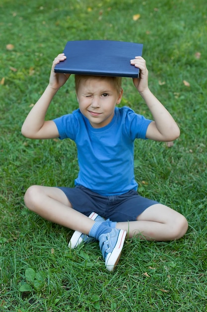 Un petit garçon dans le parc se tient debout et tient un livre sur la tête Lire un livre