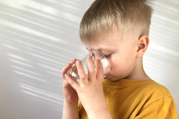 petit garçon dans un t-shirt jaune boit de l'eau