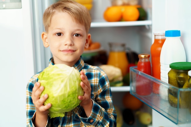 Petit garçon debout devant un réfrigérateur ouvert et choisir la nourriture