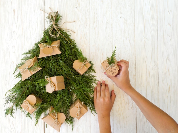 Un petit garçon décore un arbre de Noël avec des cadeaux en papier kraft