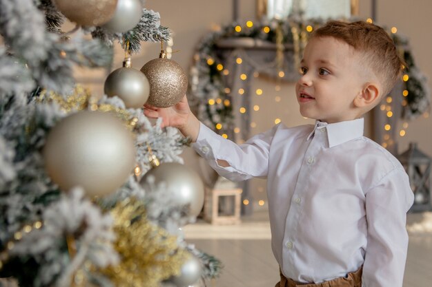 Le petit garçon décore un arbre de Noël pour Noël.