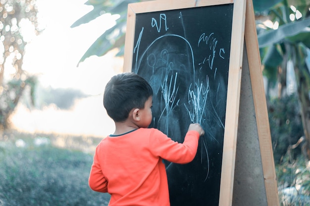 Petit garçon dessinant sur un tableau noir. Apprendre à la maison.