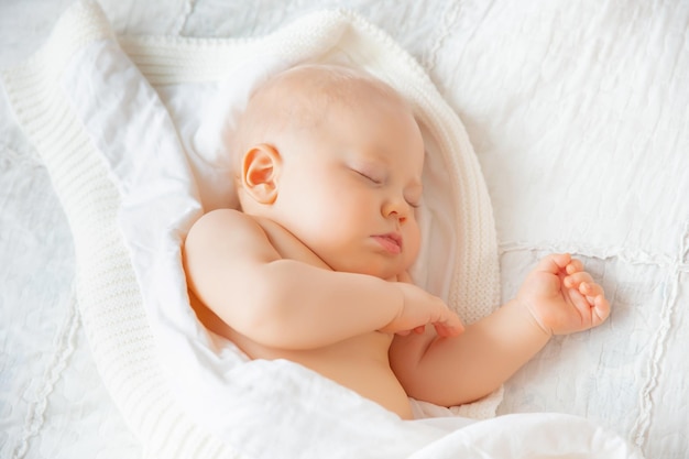 Le petit garçon dort dans la chambre sur un lit recouvert d'une couverture blanche