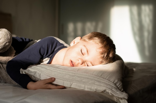 Un petit garçon dort dans son lit, le soleil brille sur lui