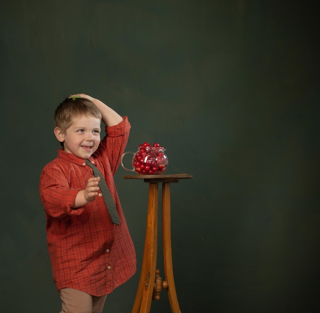 Petit garçon drôle avec des cerises sur fond de mur vert foncé