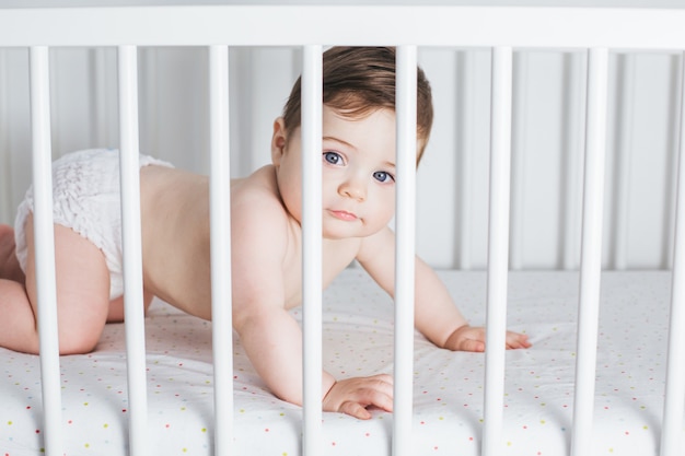 Petit garçon drôle couché dans le lit de bébé et riant