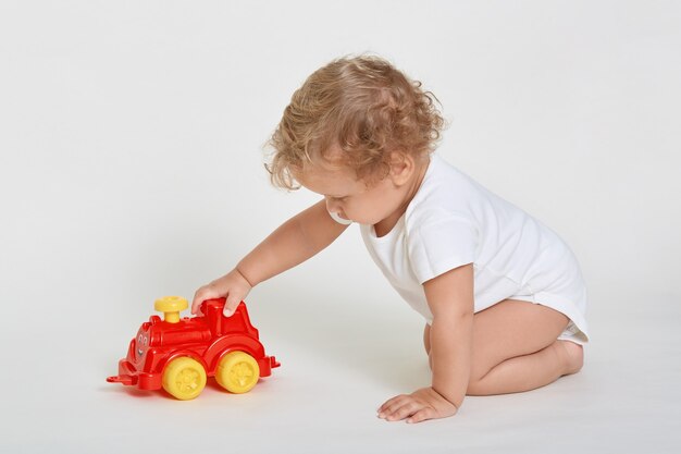 Petit garçon drôle enfant jouant avec voiture jouet rouge et jaune assis sur le sol