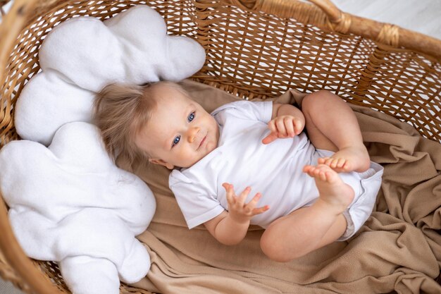 un petit garçon un enfant blond aux yeux bleus dans un body blanc se trouve sur le dos dans un berceau en osier à la maison dans la crèche un rêve d'enfant d'un enfant