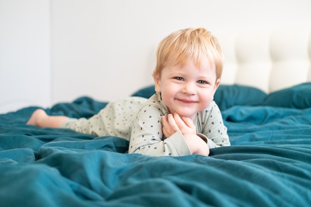 Petit garçon enfant en bonne santé en pyjama vert s'amuser au lit à la maison