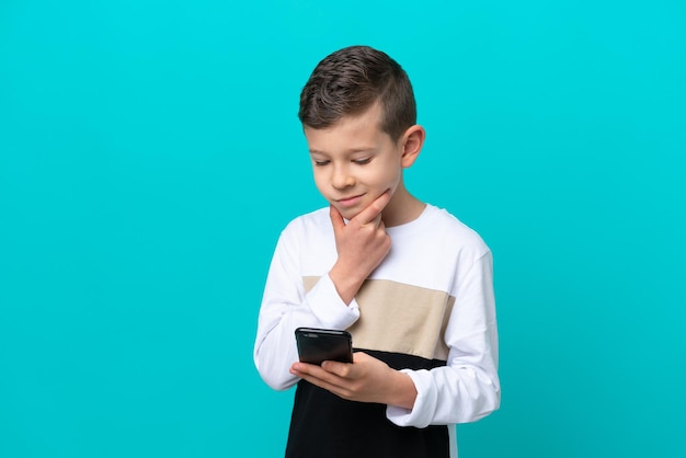 Petit garçon enfant isolé sur fond bleu pensant et envoyant un message