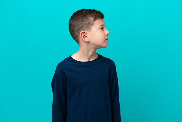 Petit garçon enfant isolé sur fond bleu regardant sur le côté